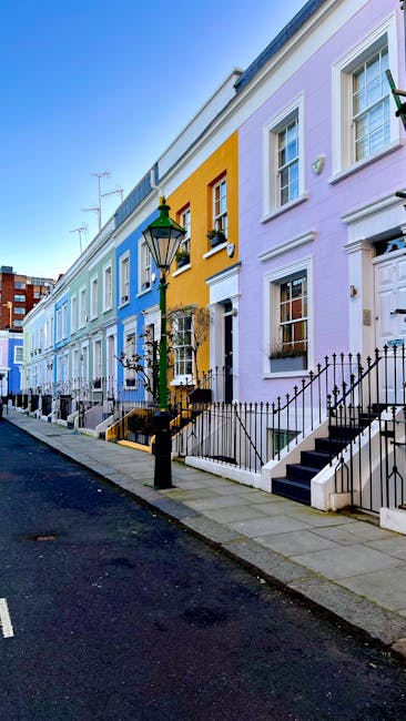 A row of multi-storey terraced houses with ornate Victorian-style facades, painted in pastel shades of pink, blue, cream, and white, featuring large sash windows, decorative moldings, and small balcon