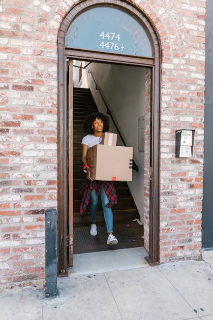 Two professional movers from Self Storage Notting Hill are inside a bright, spacious room with white walls and large arched windows allowing natural light to illuminate the space. They are carrying la