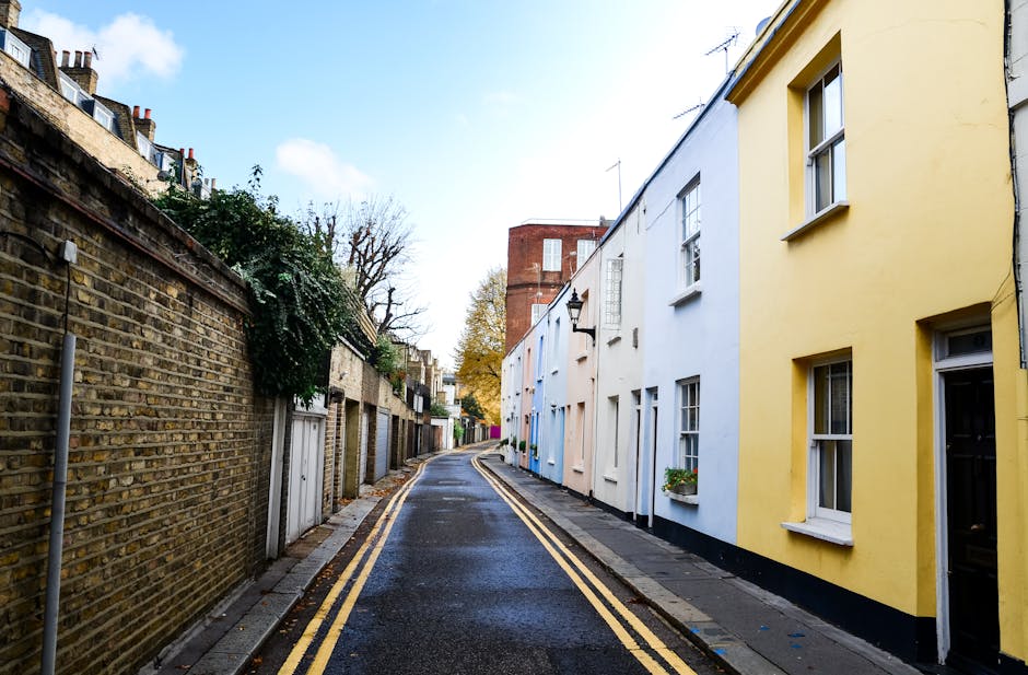 A two-storey townhouse with a pink facade, situated within a residential street. The building features large white-framed windows on the upper floor, and a smaller window on the ground floor next to a