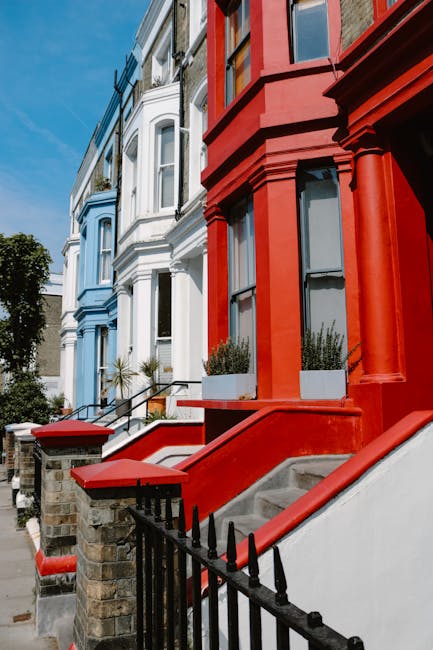 A row of multi-story residential buildings with ornate bay windows and decorative trim, painted in various colours including light blue, beige, and bright green, situated along a street in Notting Hil